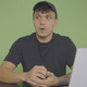 A young man sits in front of a green screen.